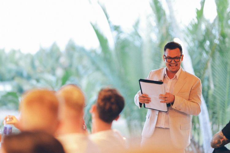 a man in a suit holding a clipboard and speaking to an audience
