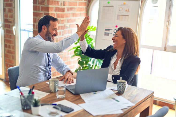Two business workers working together, giving each other a high-five at the office.