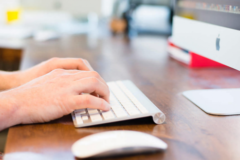 Typing on a keyboard in front of computer screen.