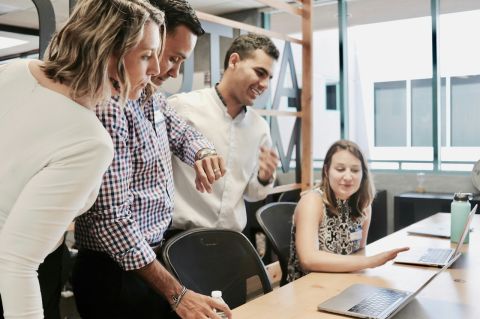 a group of four office workers gathered around a laptop