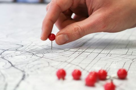 a person's hand placing a push-pin into a city street map