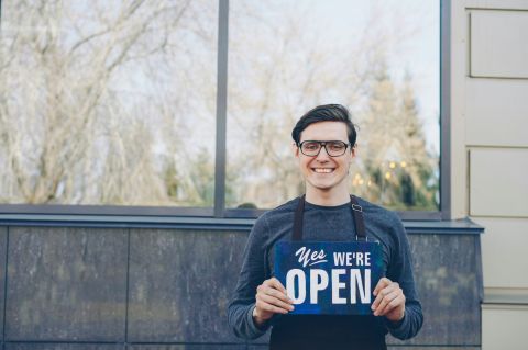 a smiling man holding a sign that says "Yes, We're Open"
