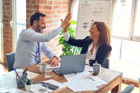 Two business workers working together, giving each other a high-five at the office.