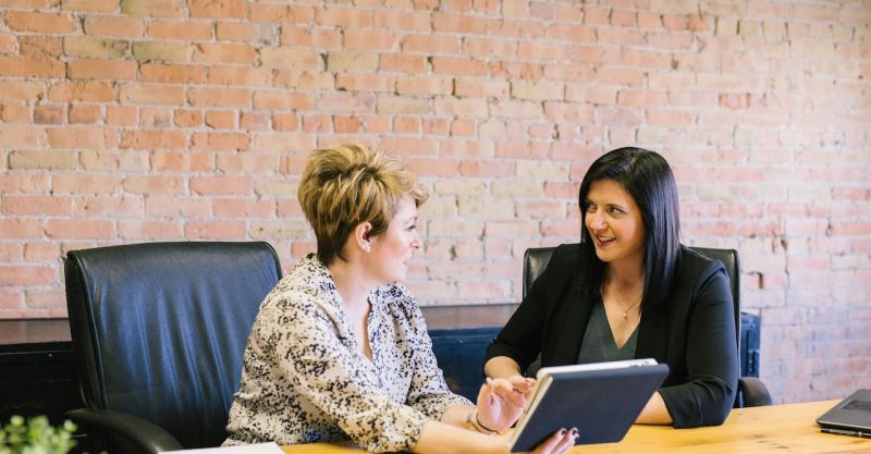 two women talking, sitting at a conference table