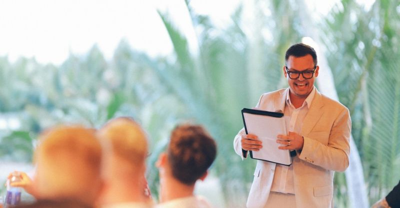 a man in a suit holding a clipboard and speaking to an audience