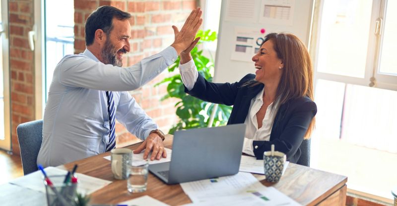 Two business workers working together, giving each other a high-five at the office.