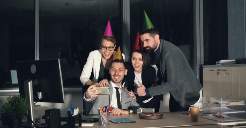 a group of coworkers wearing party hats taking a selfie