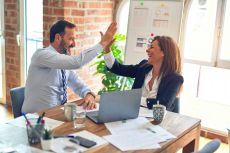 Two business workers working together, giving each other a high-five at the office.