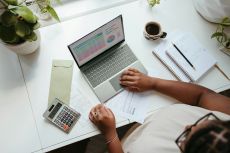 Close-up of hands using calculator and laptop on white desk, concept of finance, budgeting, and business work