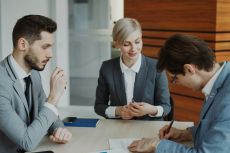 Young businessman in suit signing contract with his colleague while corporate lawyer explaining details of partnership sitting in modern office indoors